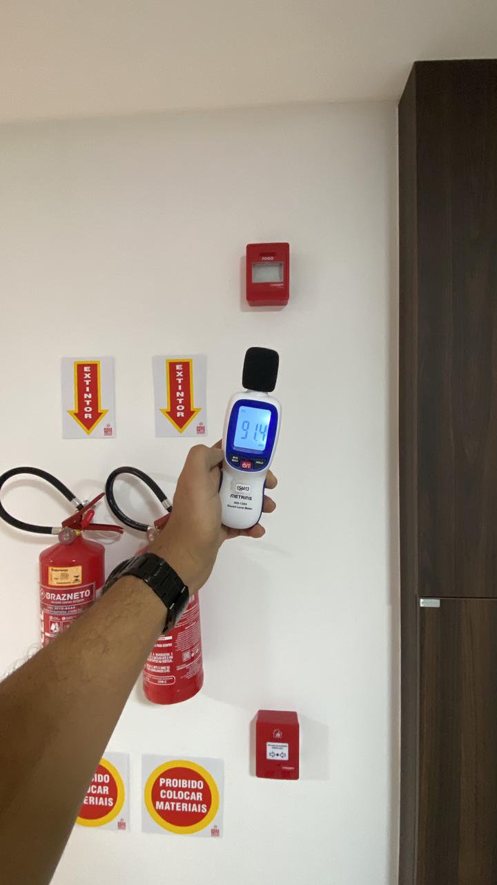 Técnico medindo nível sonoro de sirene do sistema de alarme de incêndio com decibelímetro